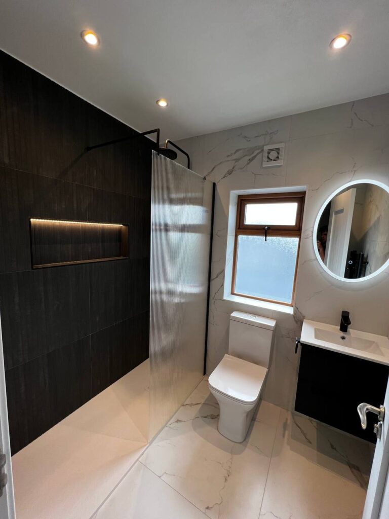 An image of a shower and toilet bowl beside the bathroom sink and mirror