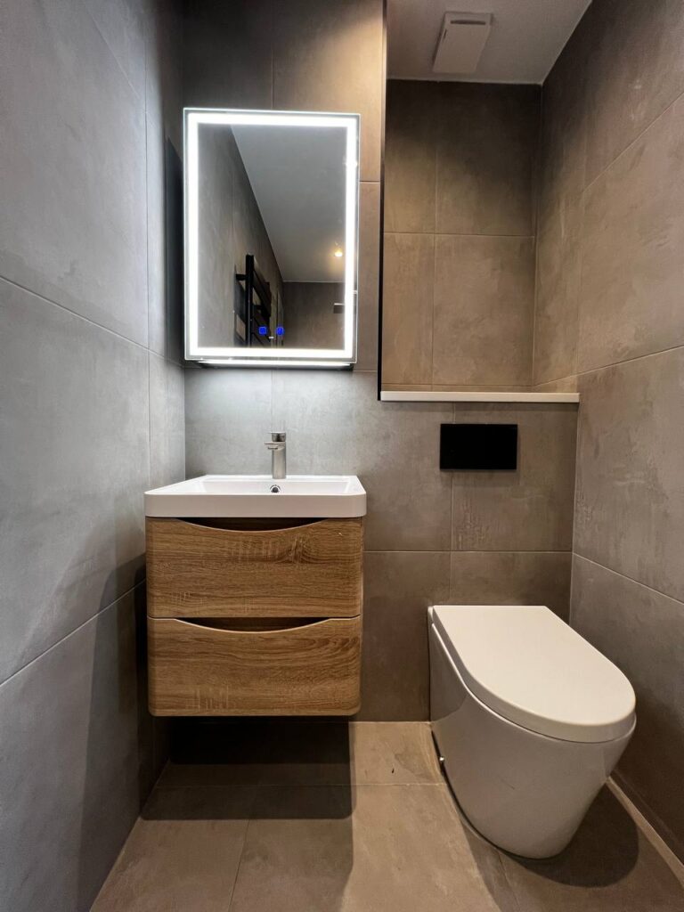 An image of a toilet bowl beside a mirror above the bathroom sink